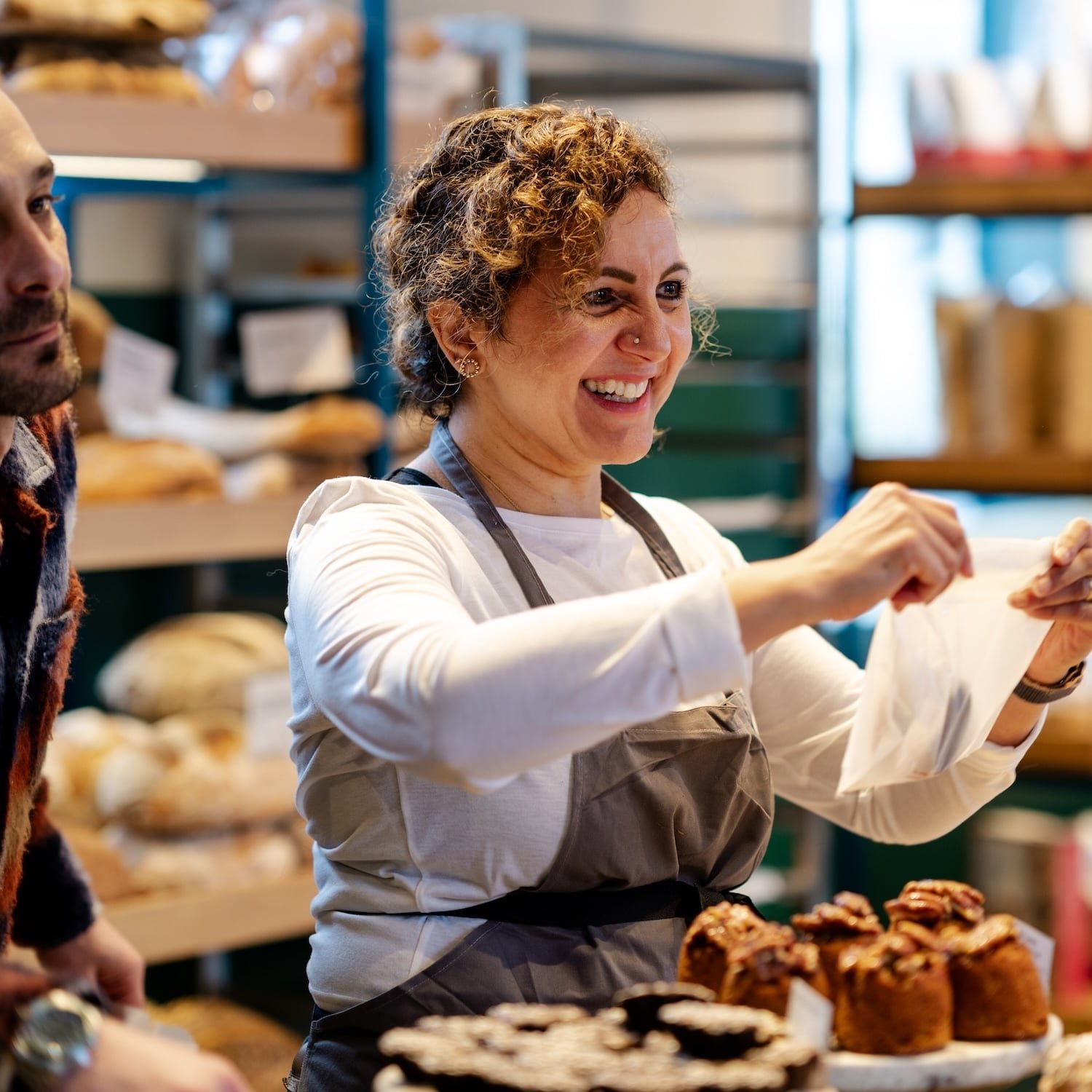 Smiling woman holding a bag, baked goods in front.