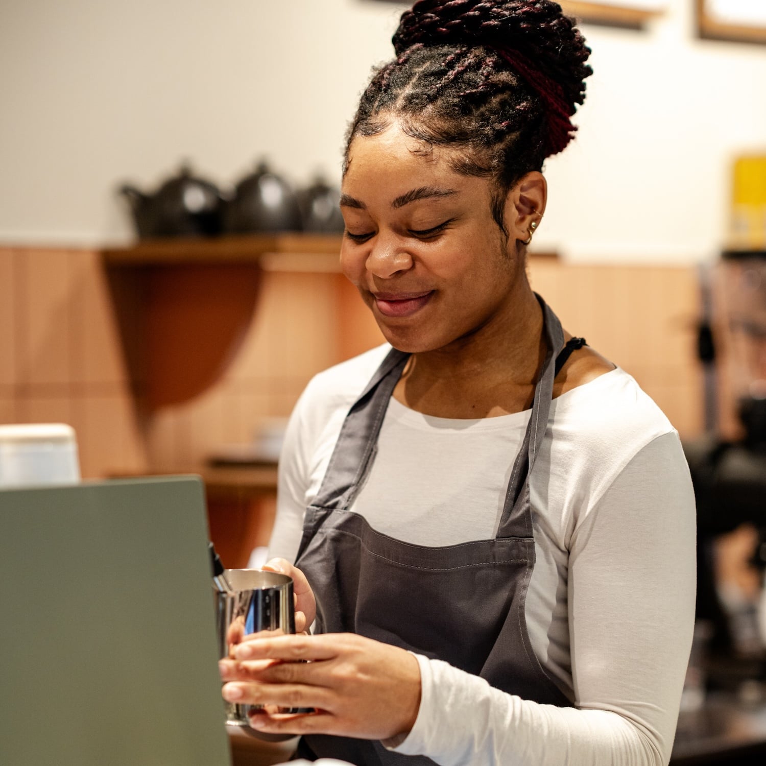 Woman with dreadlocks, wearing apron, holding a metal pitcher.