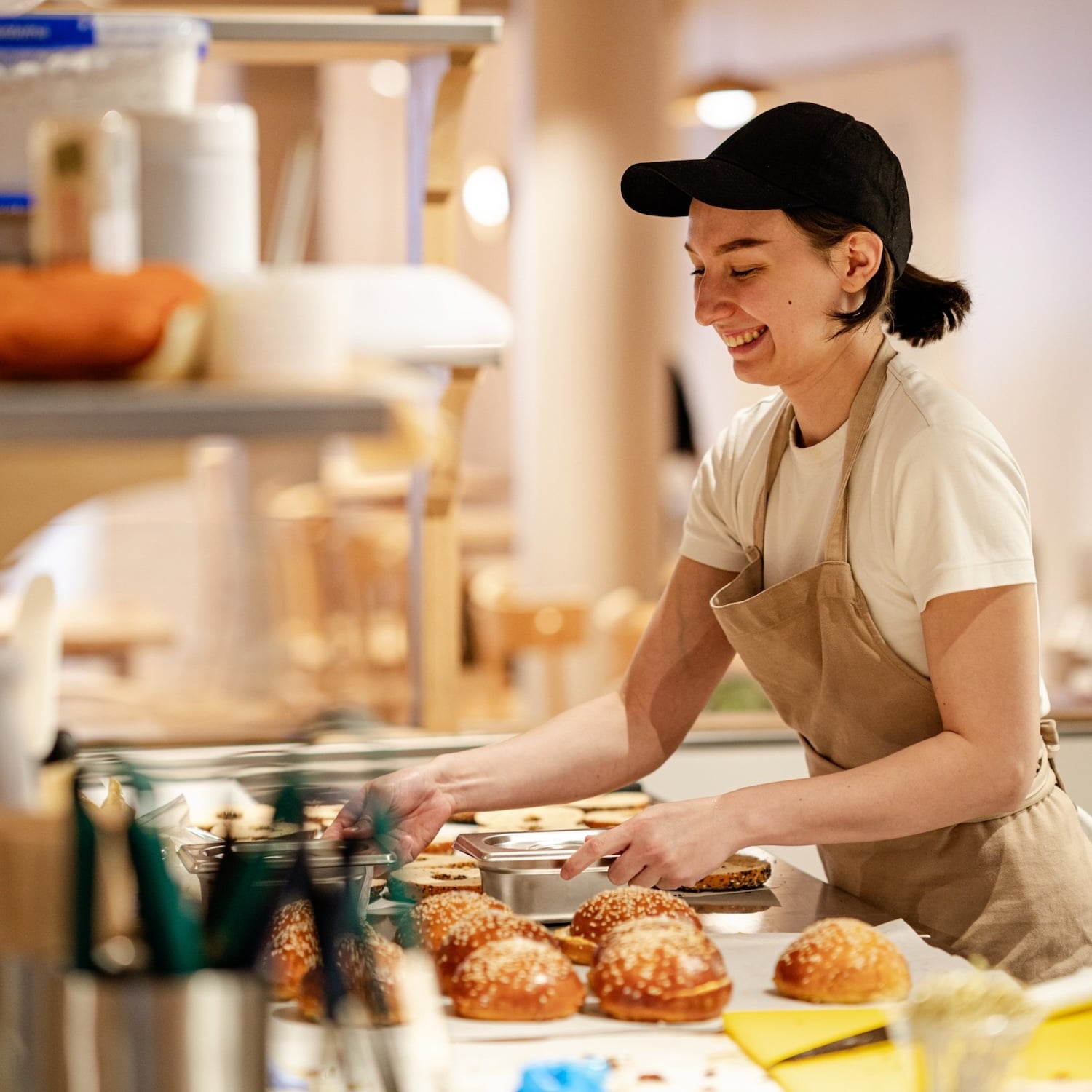 Woman in apron and cap, smiling, with baked goods.
