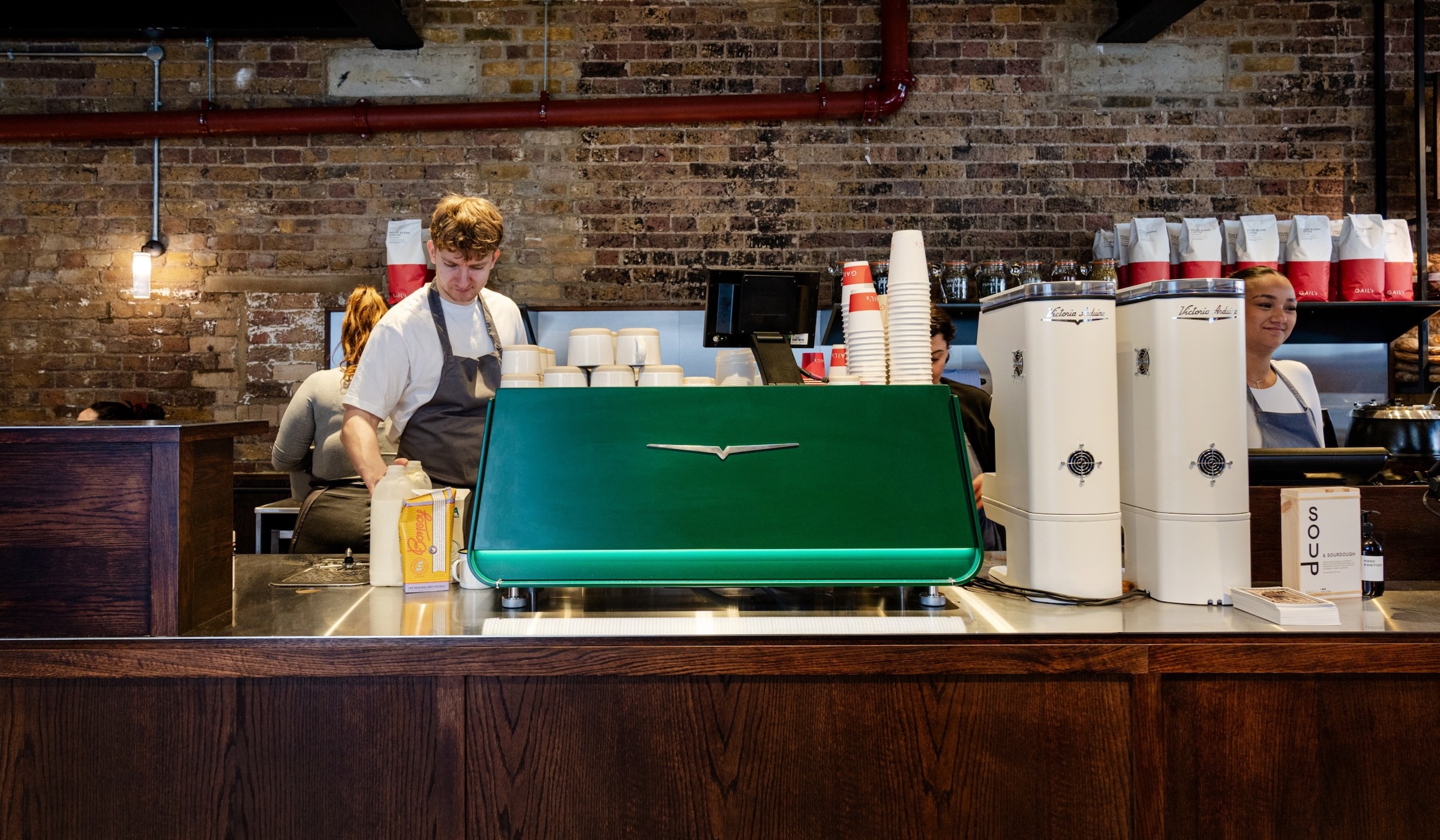 Baristas at work, coffee machine, brick wall.