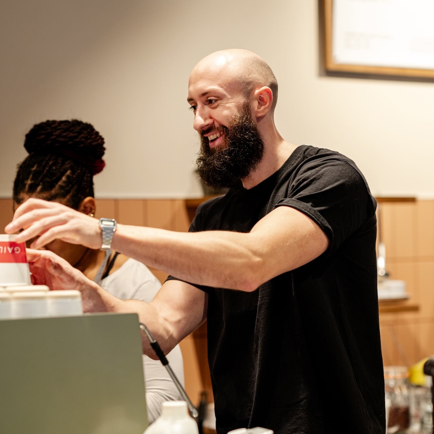 Bald barista with a beard smiling, preparing coffee.