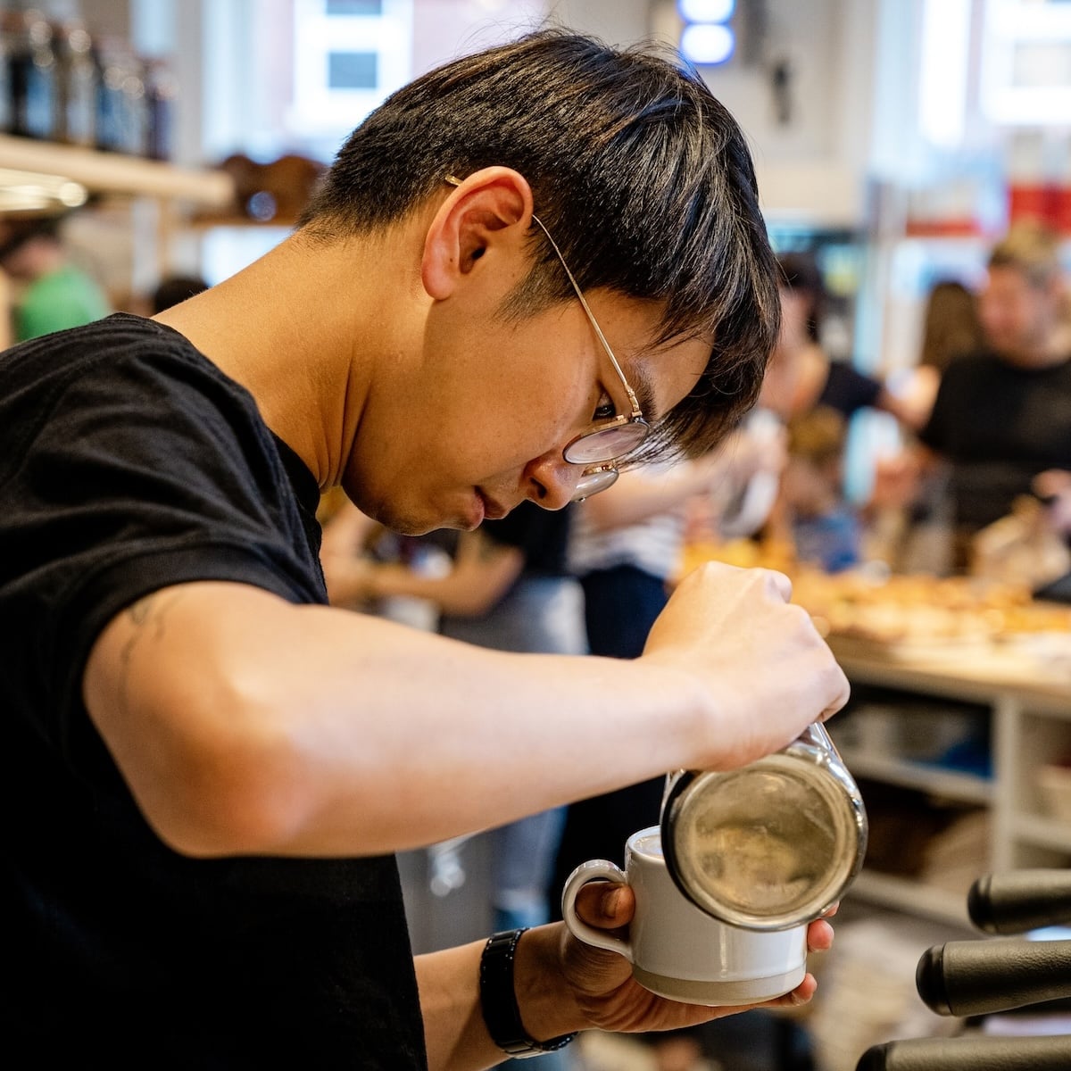 Barista pouring milk into a mug, action shot.