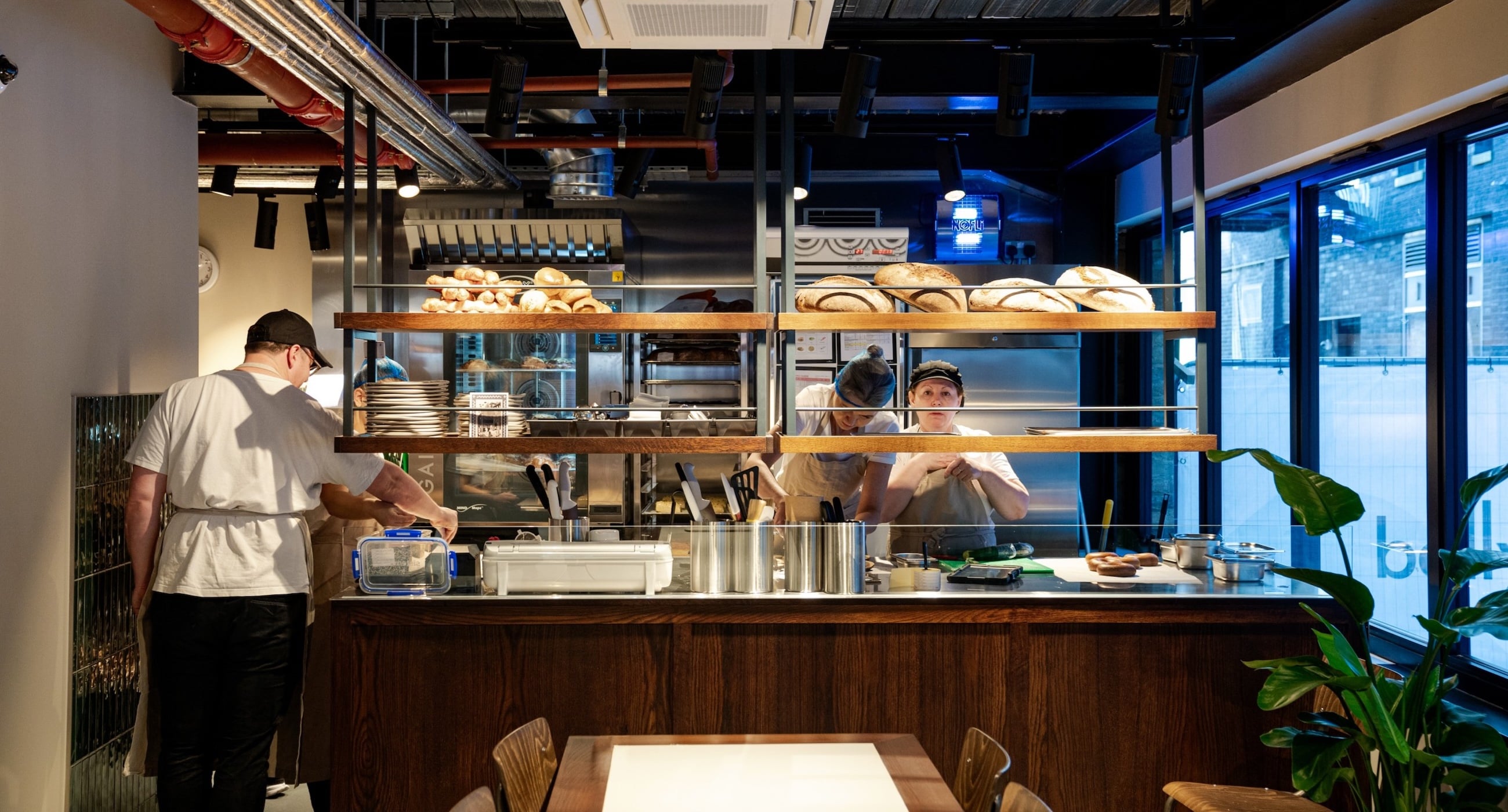 Workers preparing food in a bakery kitchen with bread on shelves.