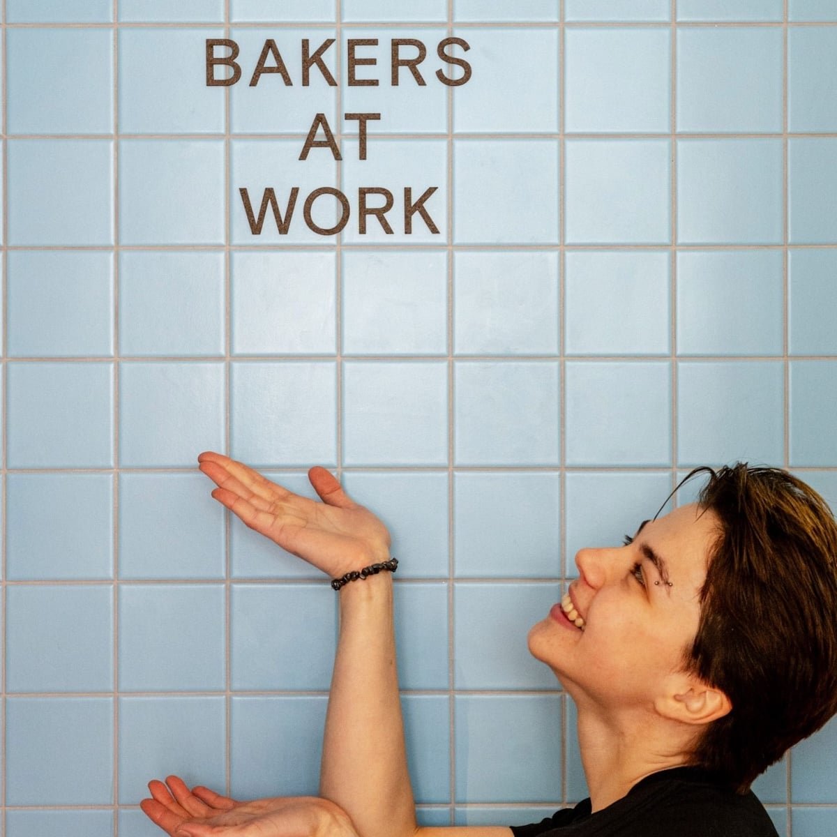 Person pointing at "Bakers at Work" text on a blue tiled wall.