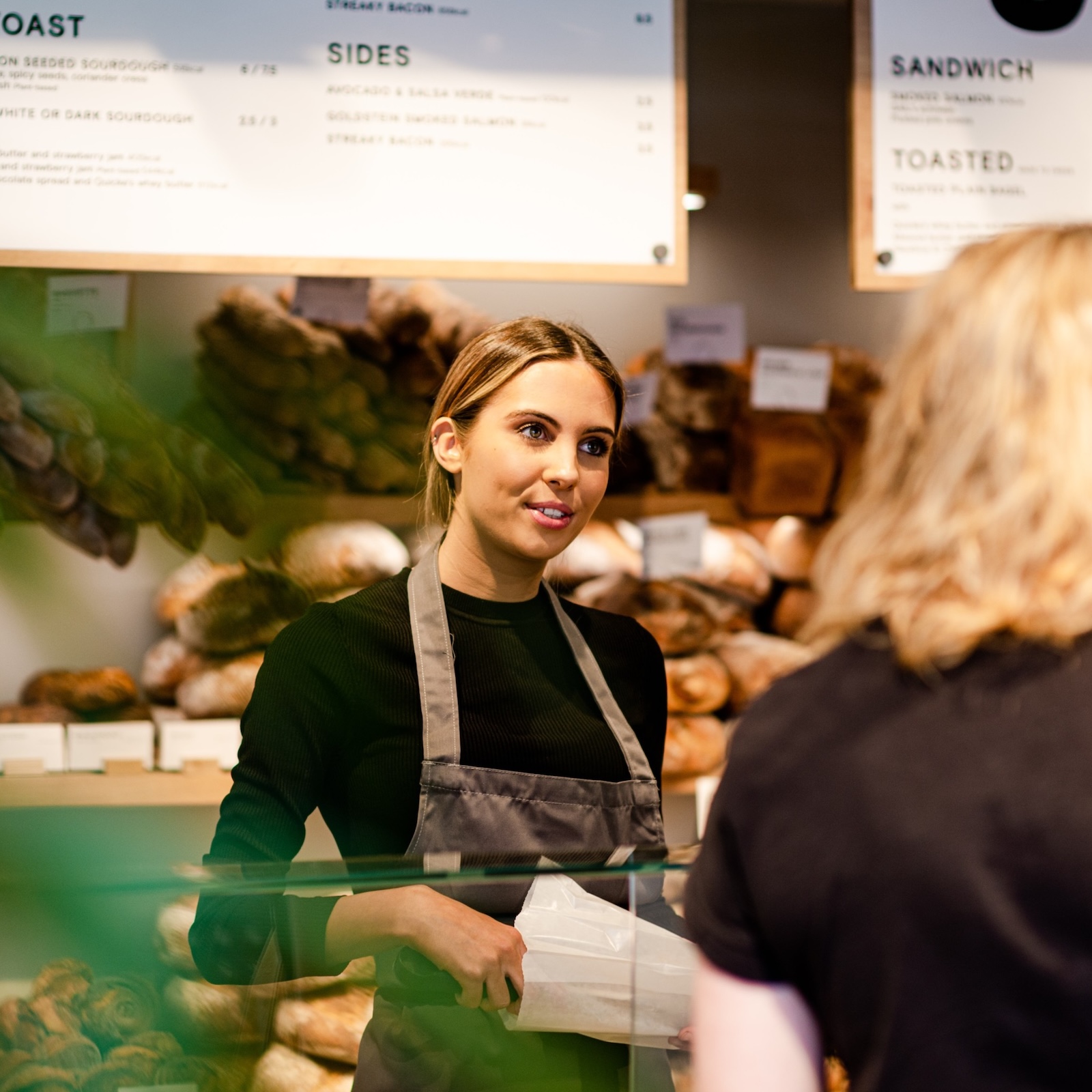 Woman serving a customer at a bakery, holding a bag.