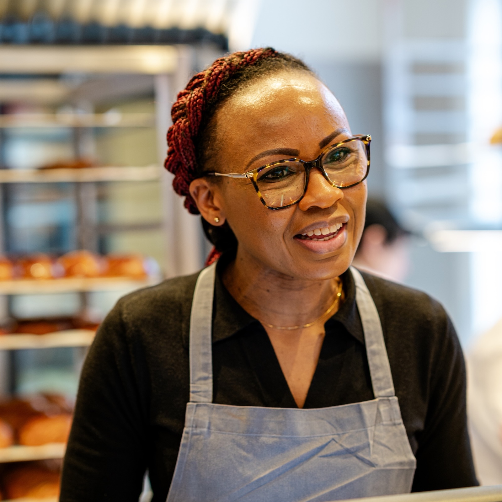 Woman wearing glasses and apron in a bakery.