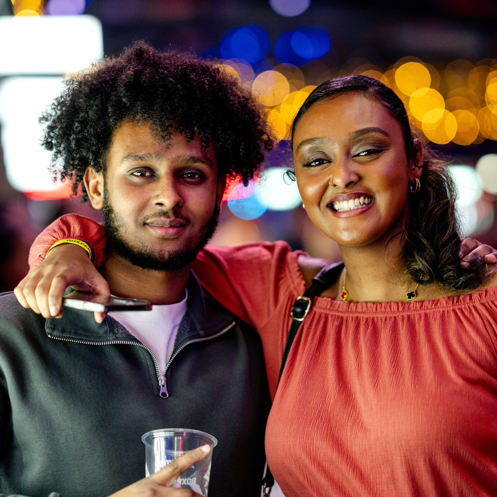 Smiling couple posing for a photo, with blurred lights in the background.