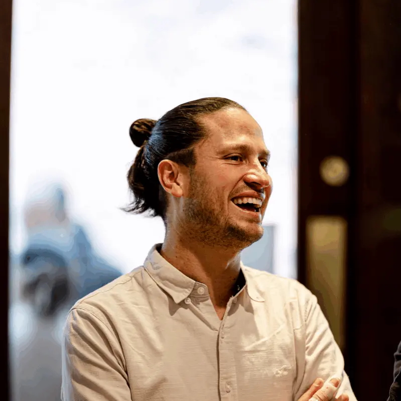 Man with long hair smiling, wearing a button-down shirt.