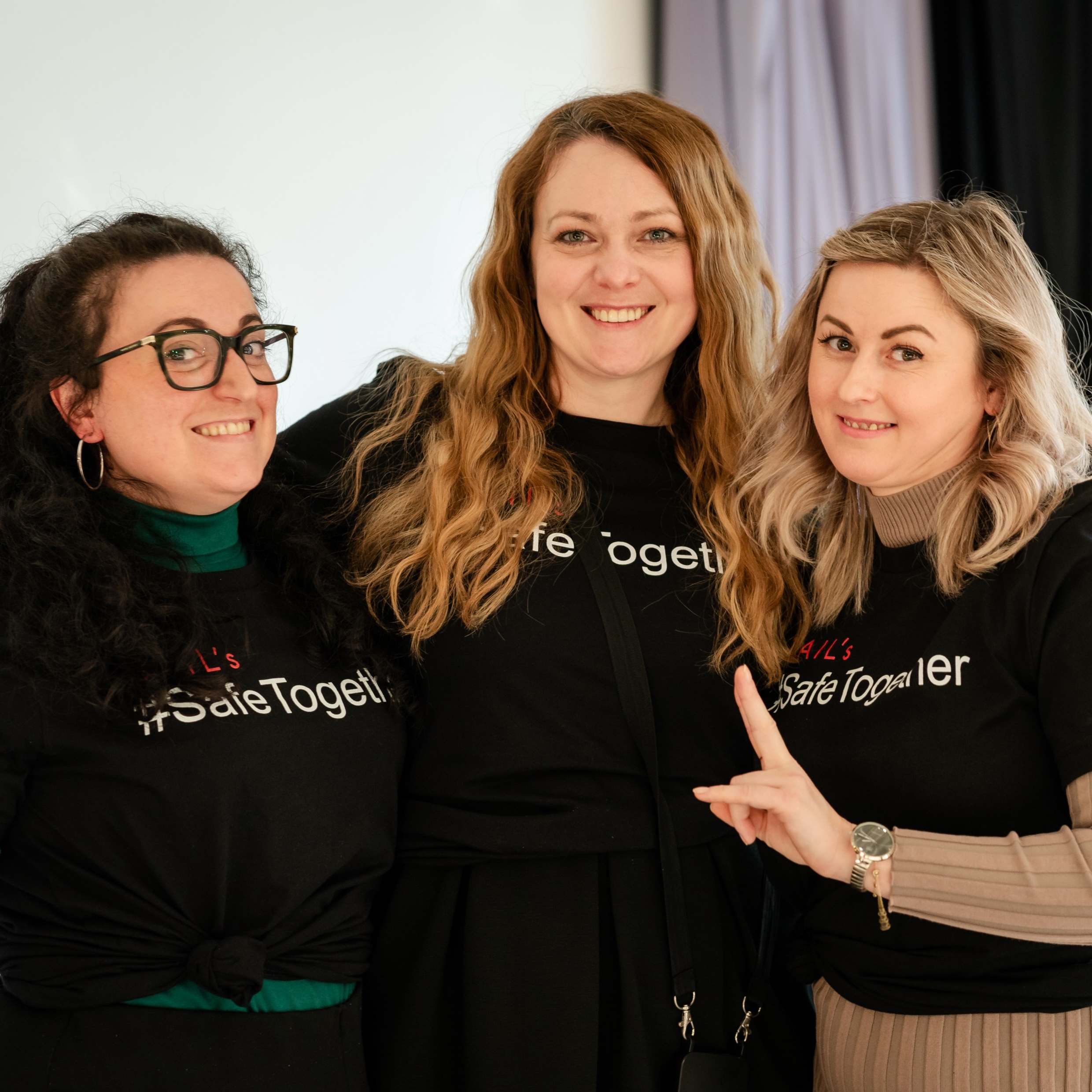 Three women smiling, wearing black shirts with "Safe Together" on them.