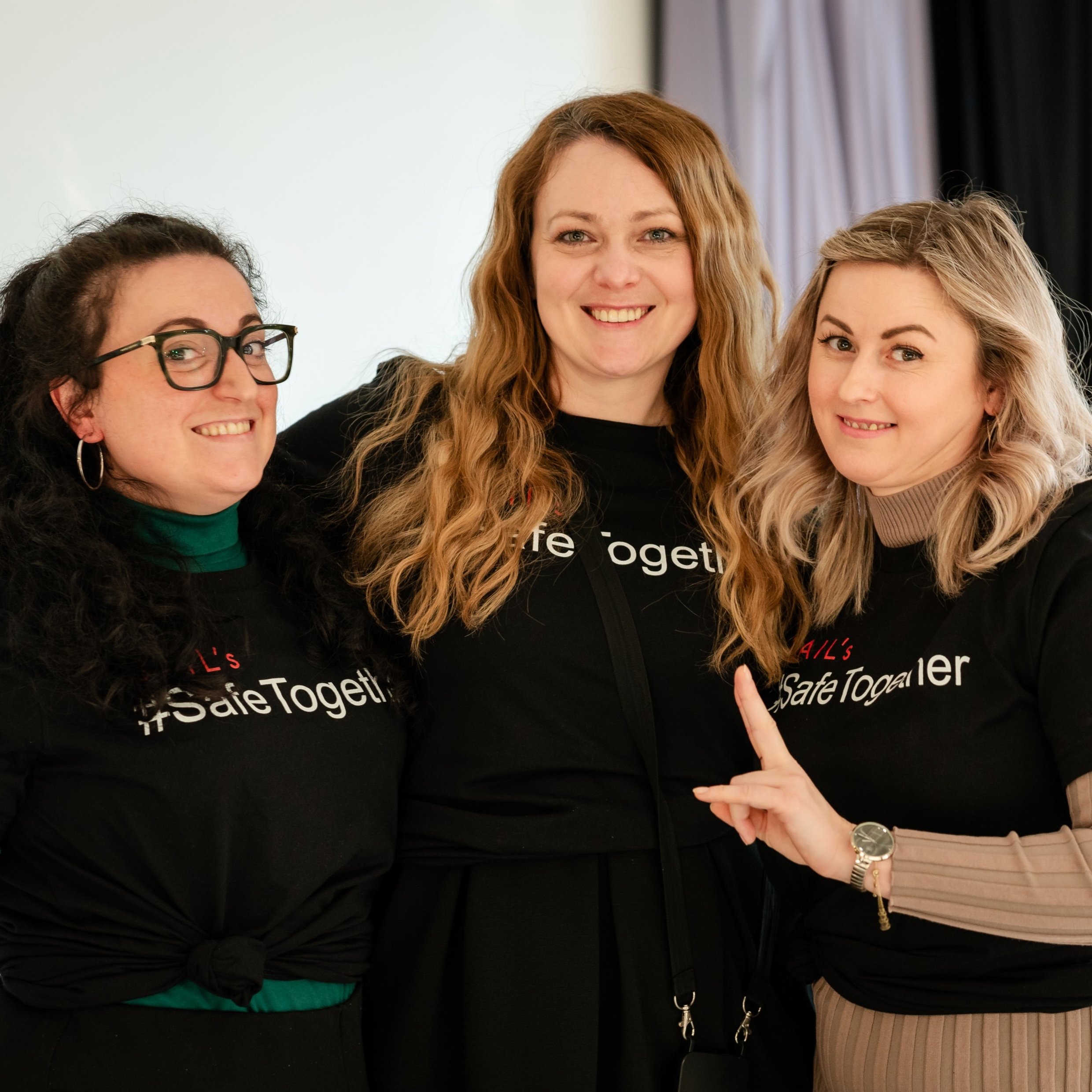 Three women smiling, wearing black shirts with "Safe Together" on them.