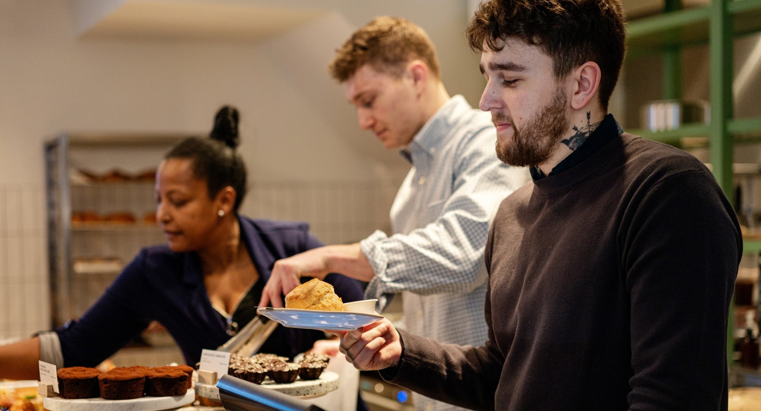 People at a bakery counter, selecting pastries.