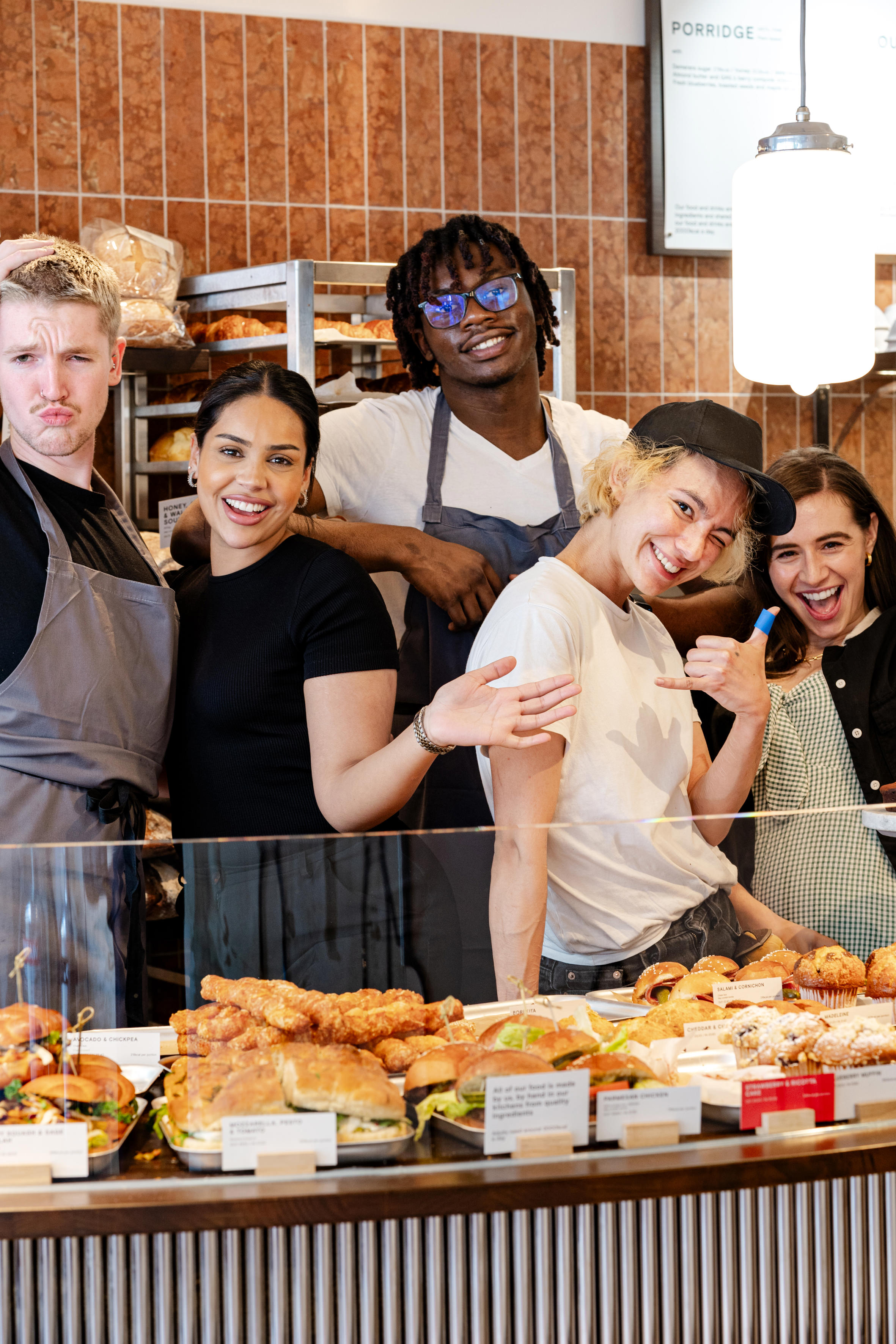 Group of smiling bakery staff behind a display of baked goods.