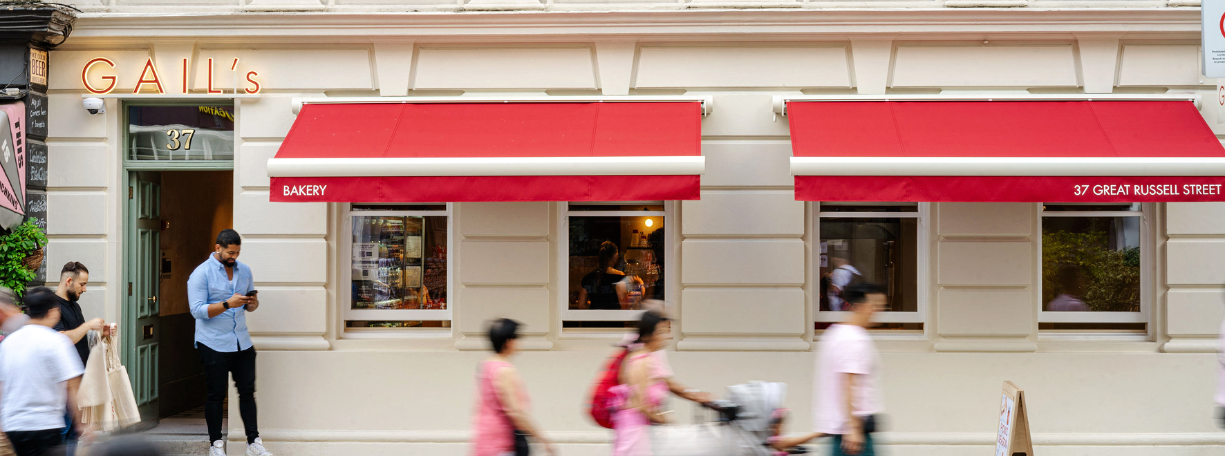 Exterior of Gail's Bakery with red awnings and people walking by.