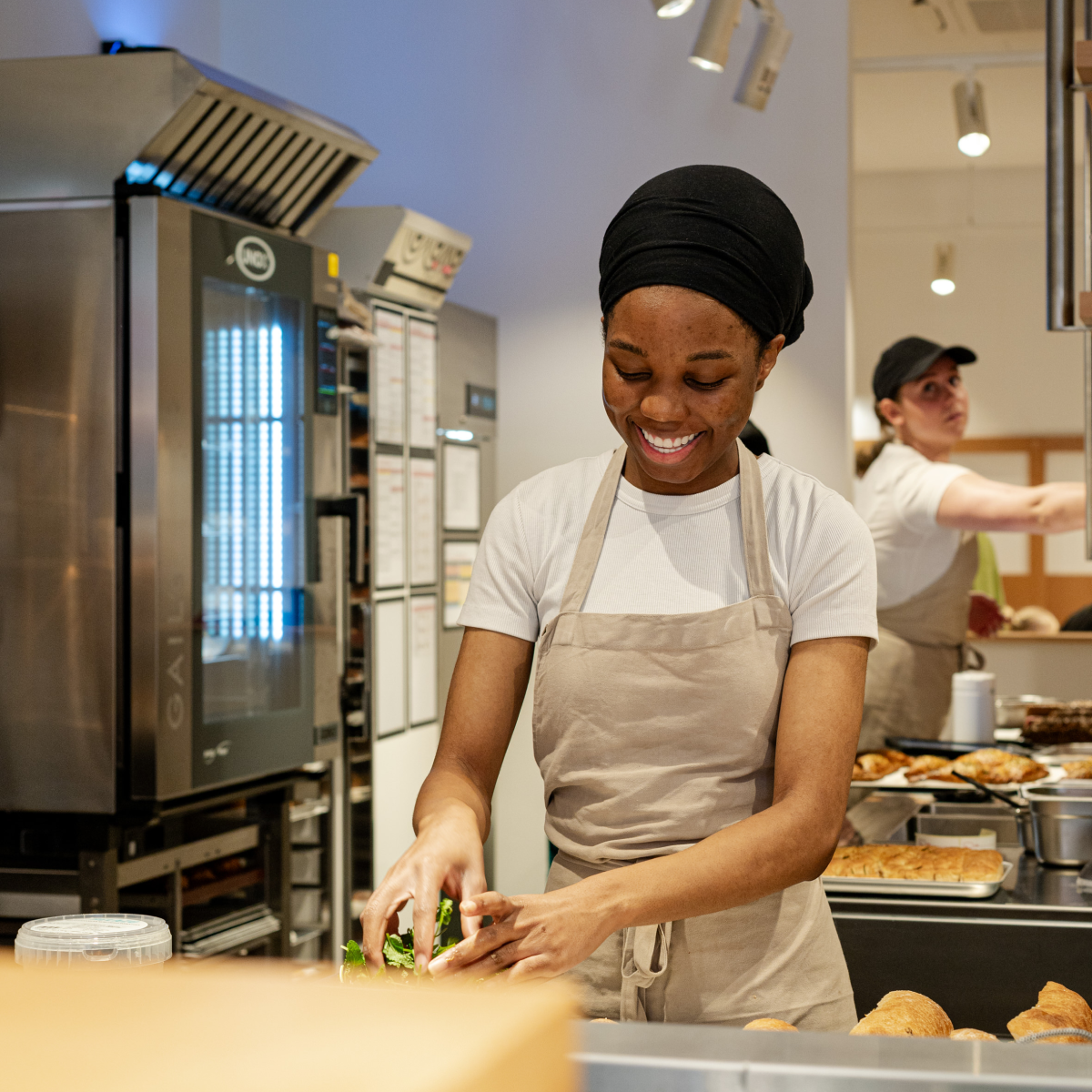 Woman preparing food in a bakery, smiling.