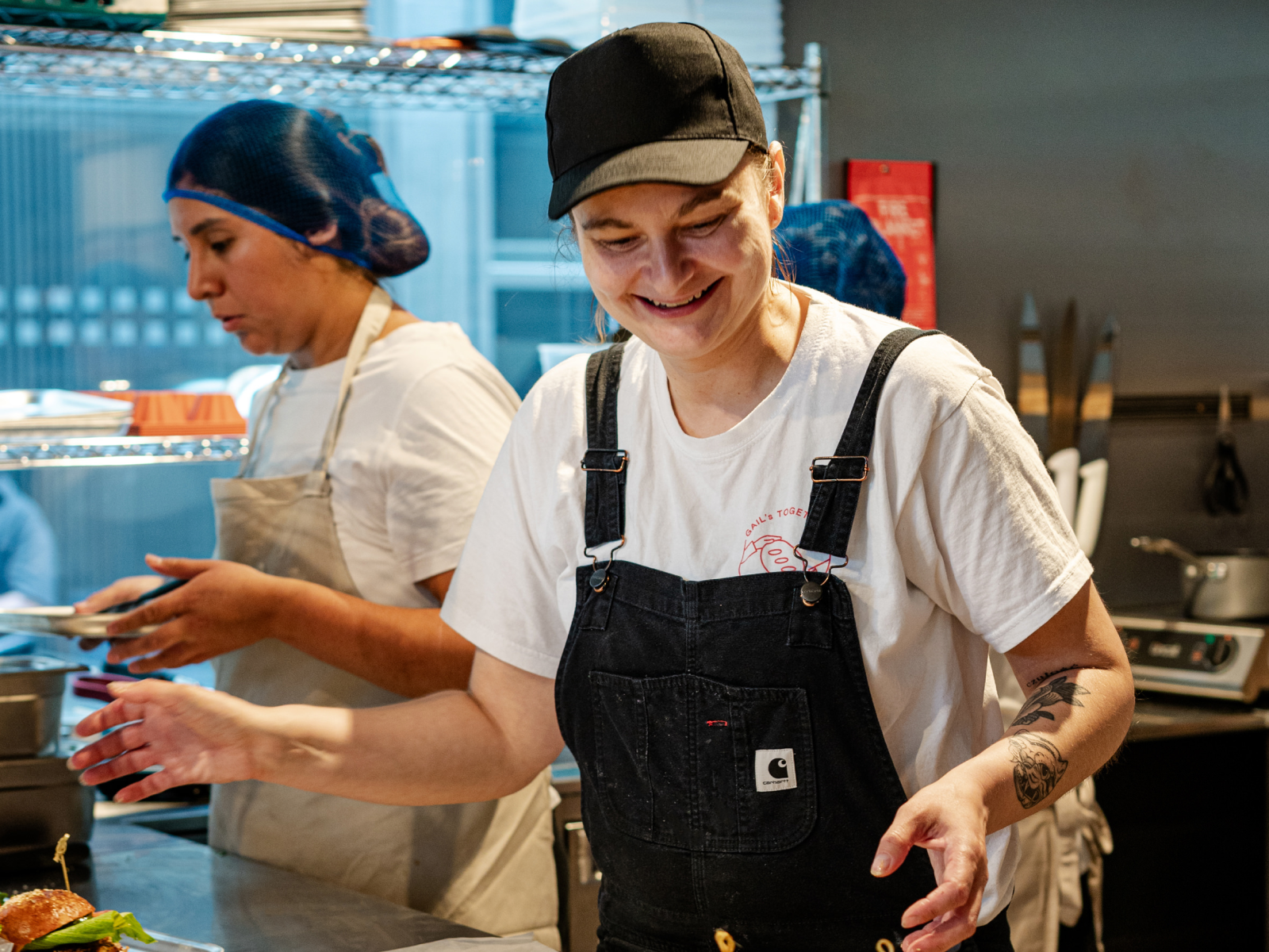 Chefs preparing food in a commercial kitchen. One chef smiles.