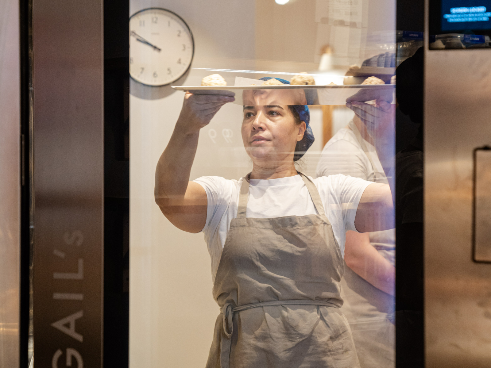 Woman holding tray of baked goods, wearing apron.