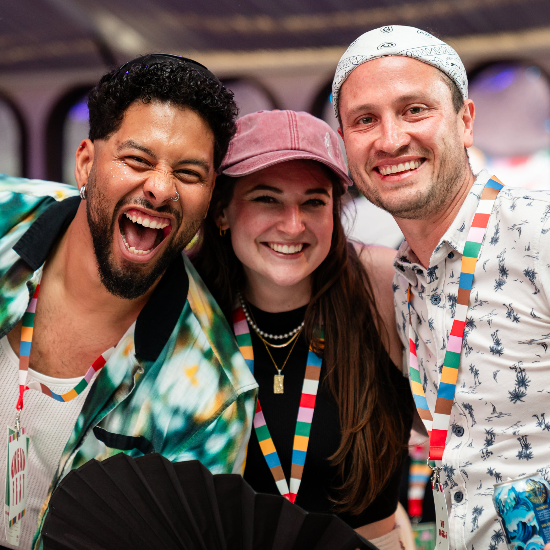 Three smiling people, festival attire, colorful lanyards.