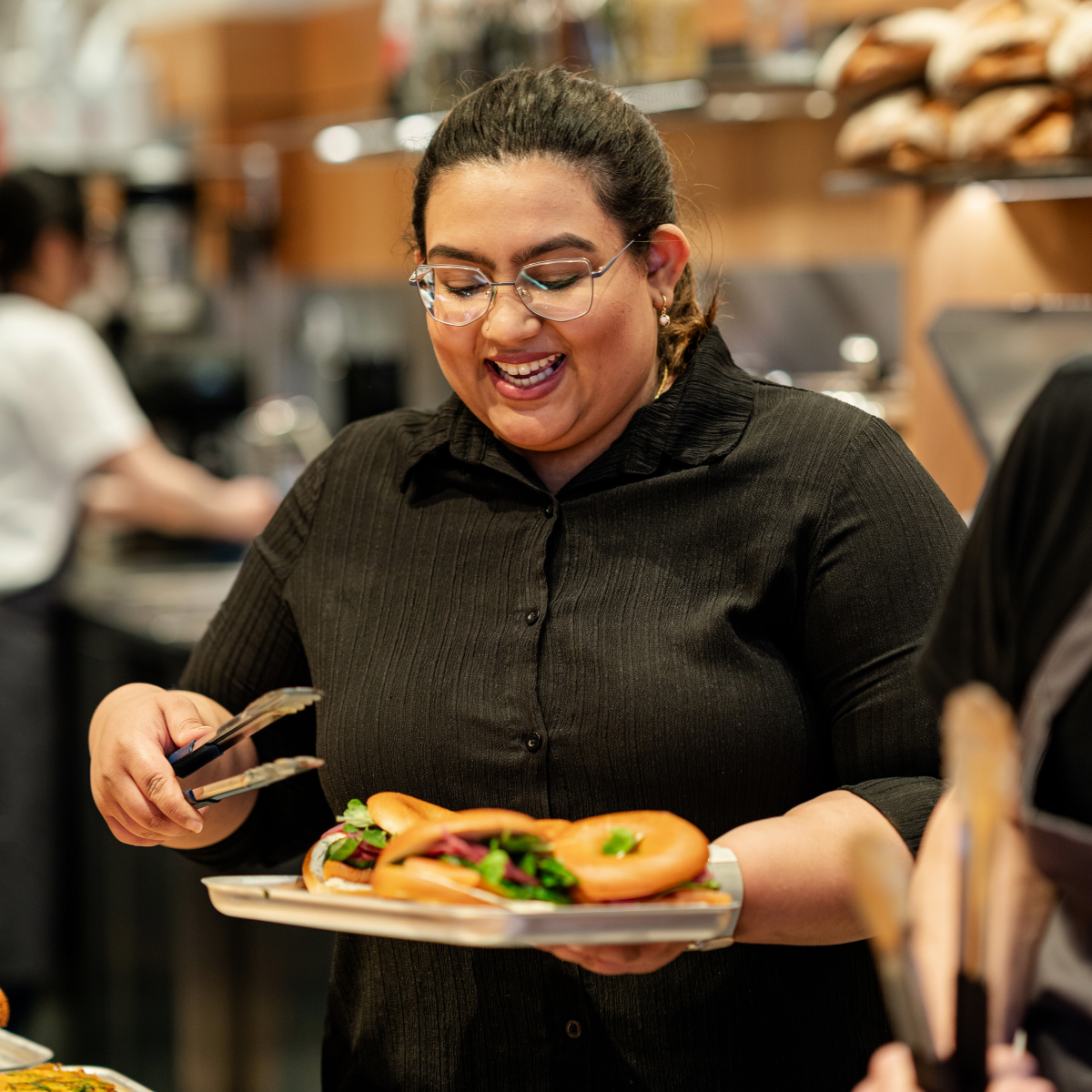 Woman holding tray of food with tongs, smiling.