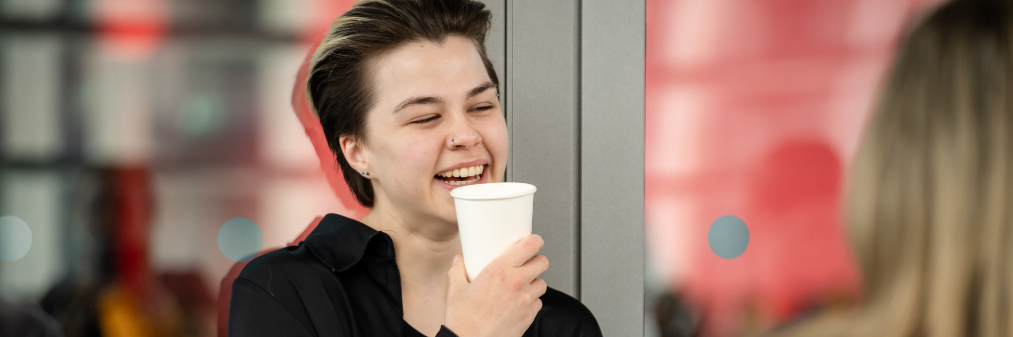 Person holding a coffee cup, smiling, with a blurred background.
