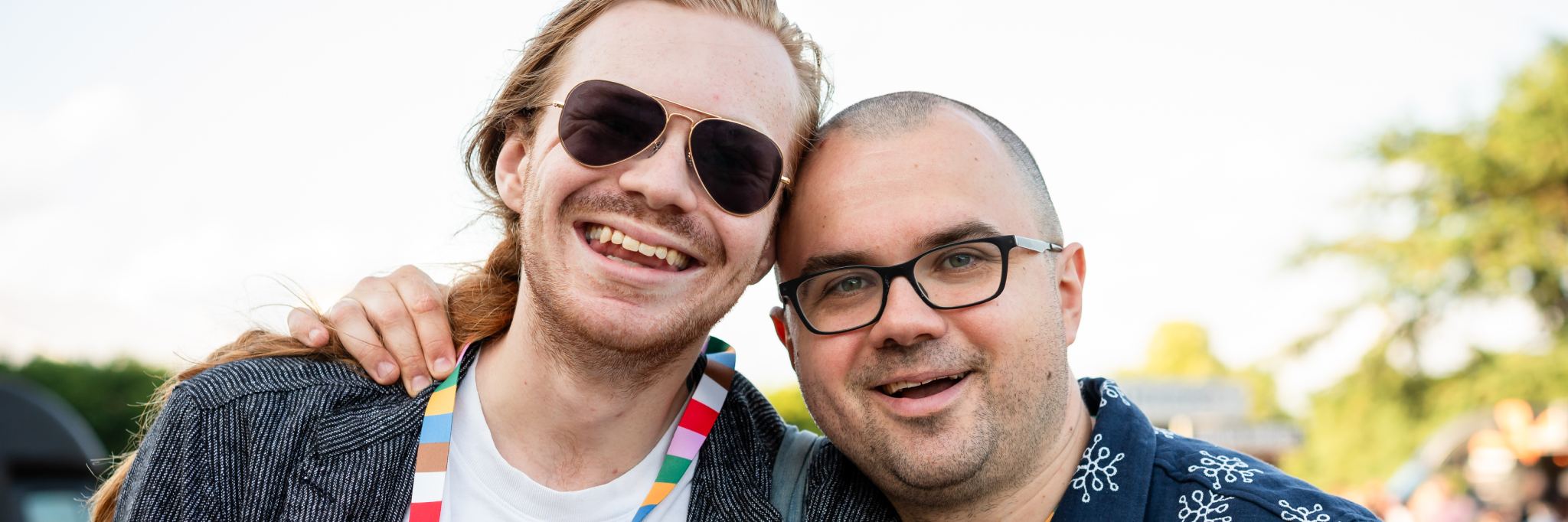 Two men smiling, one with sunglasses, the other with glasses.
