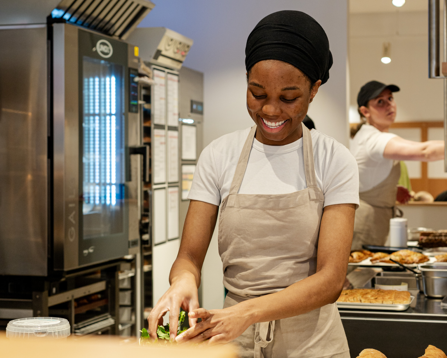 Woman preparing food in a bakery, smiling.
