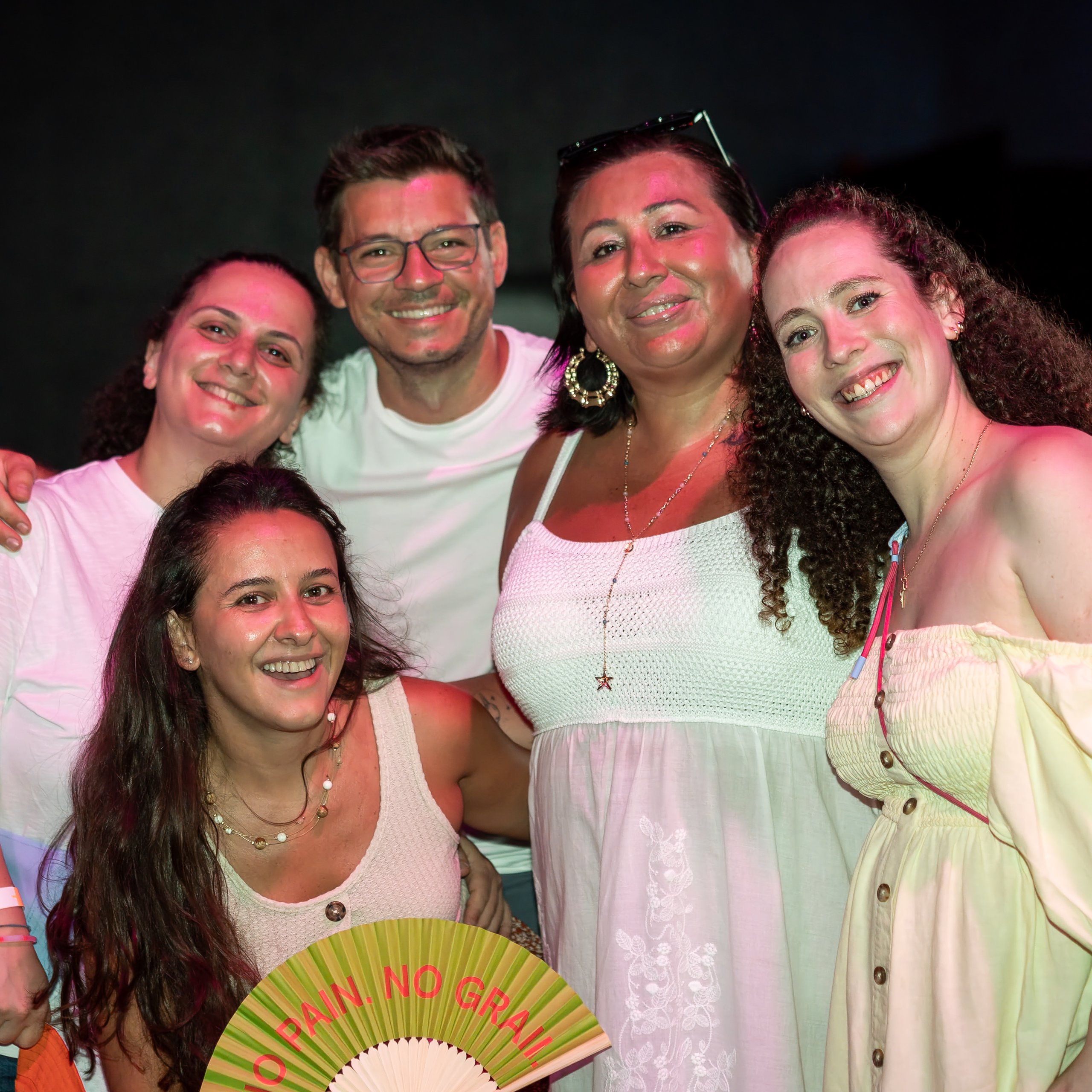 A group of five smiling people posing together at an evening event, with one holding a decorative fan.