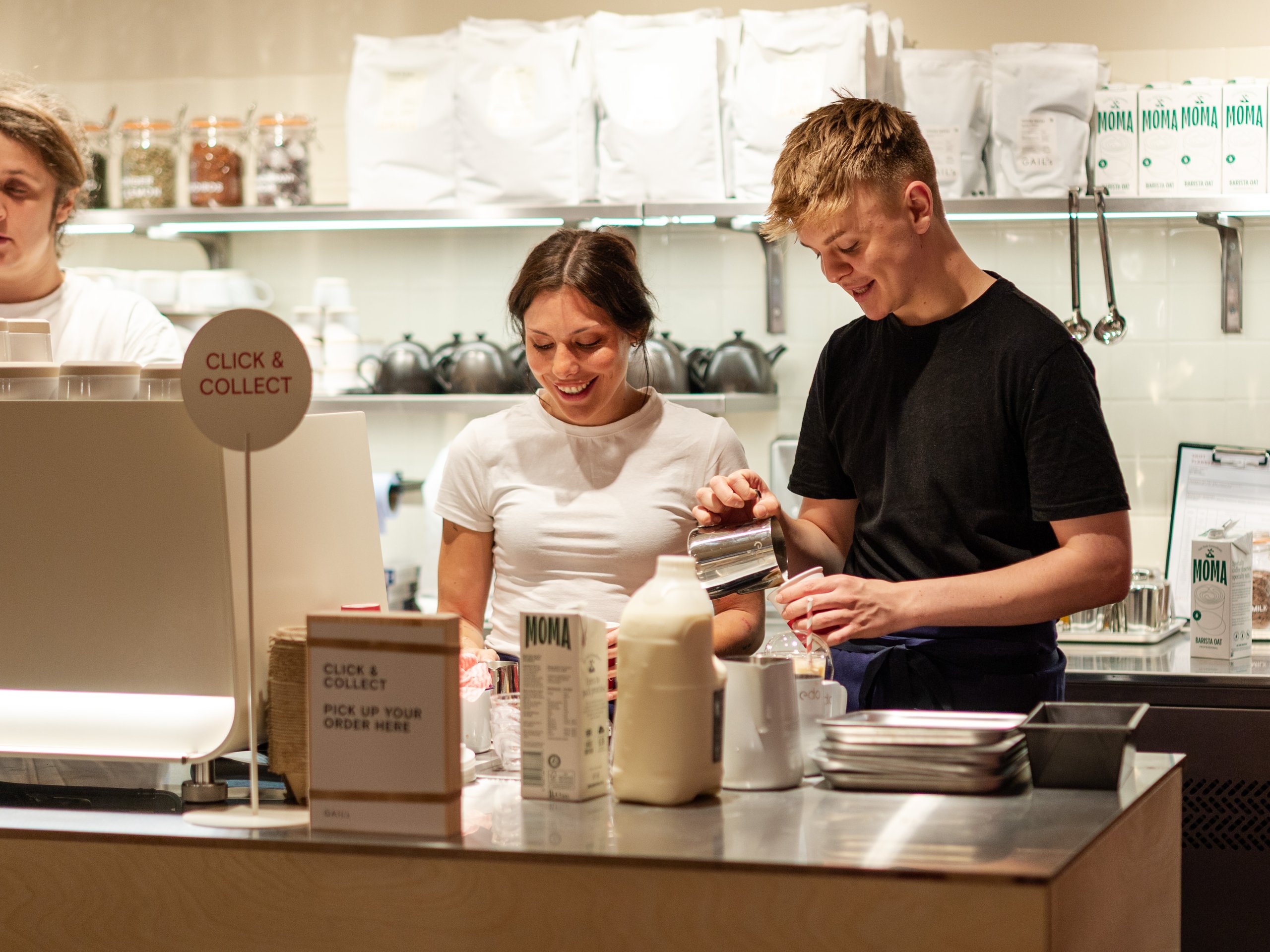A male and female barista preparing drinks behind the counter in a modern cafe.