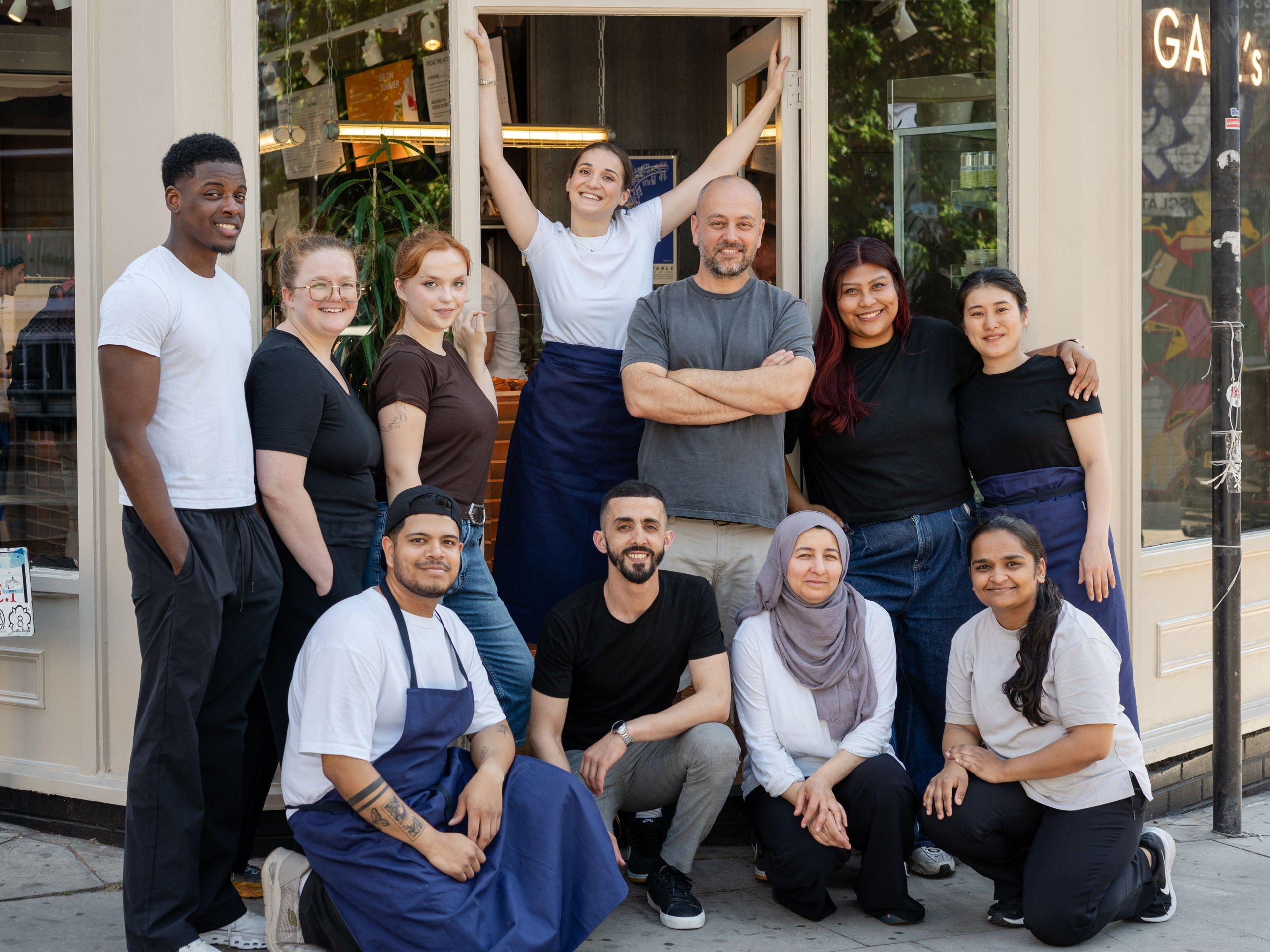 A diverse group of eleven restaurant staff members pose together outside the entrance.