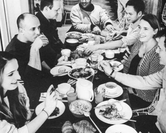 Black and white image of a group of people around a table eating and drinking.